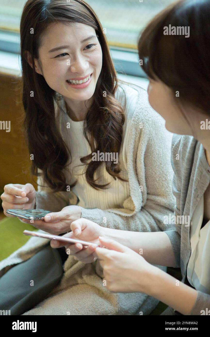 Two women in their 20s holding a smartphone and smiling Stock Photo - Alamy