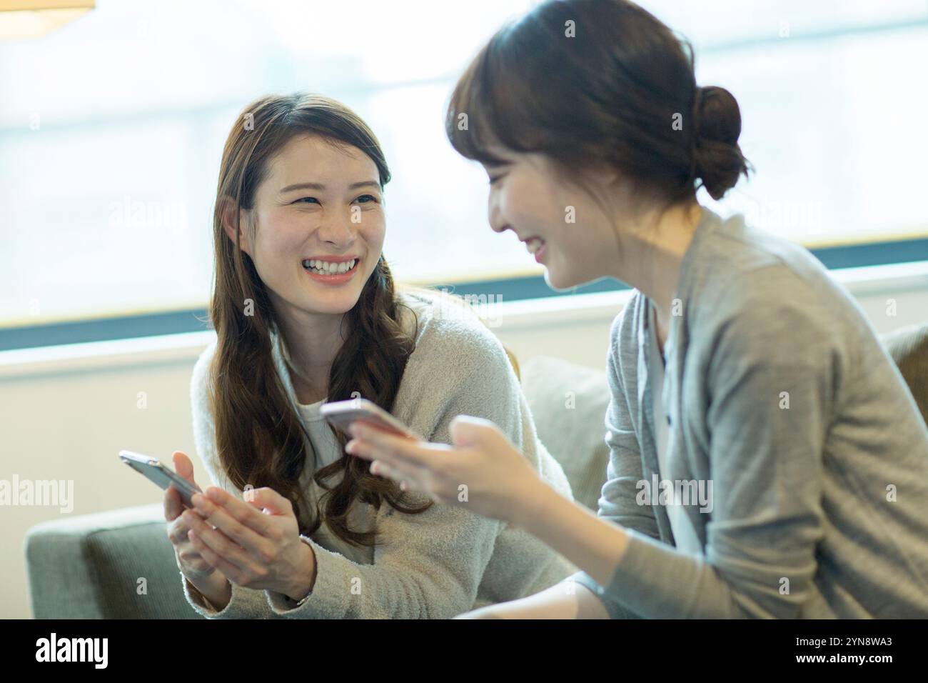 Two women in their 20s holding a smartphone and smiling Stock Photo - Alamy