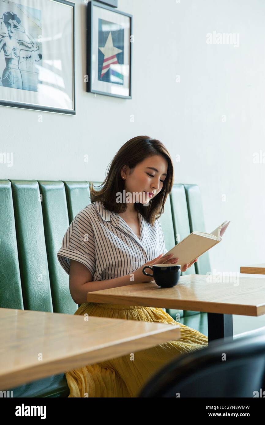 Woman in her 20s sitting by the window reading a book Stock Photo - Alamy