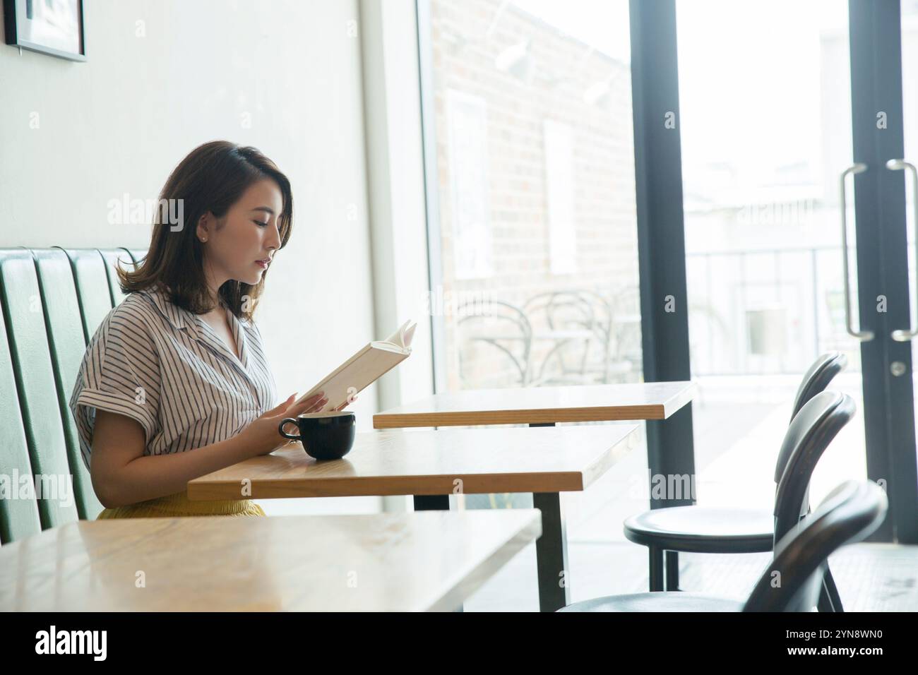 Woman in her 20s sitting by the window reading a book Stock Photo - Alamy