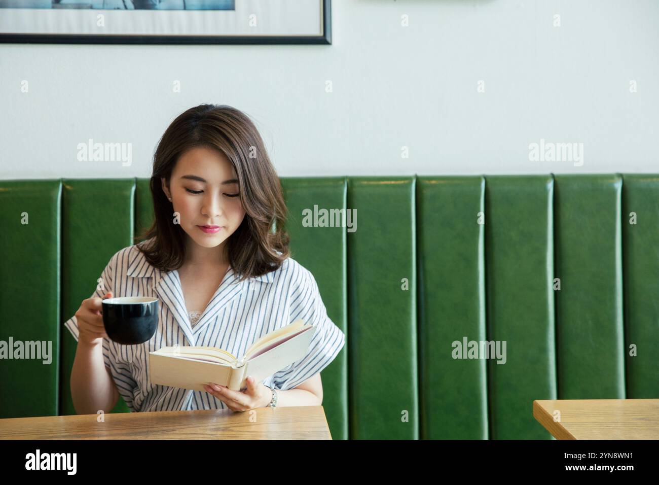 Woman in her 20s sitting by the window reading a book Stock Photo - Alamy
