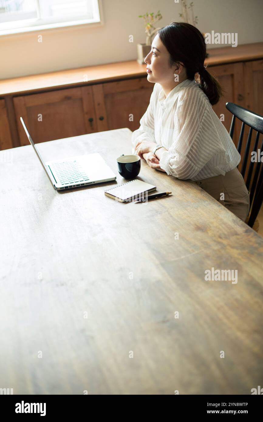Woman in her 20s looking out while working by the window Stock Photo ...