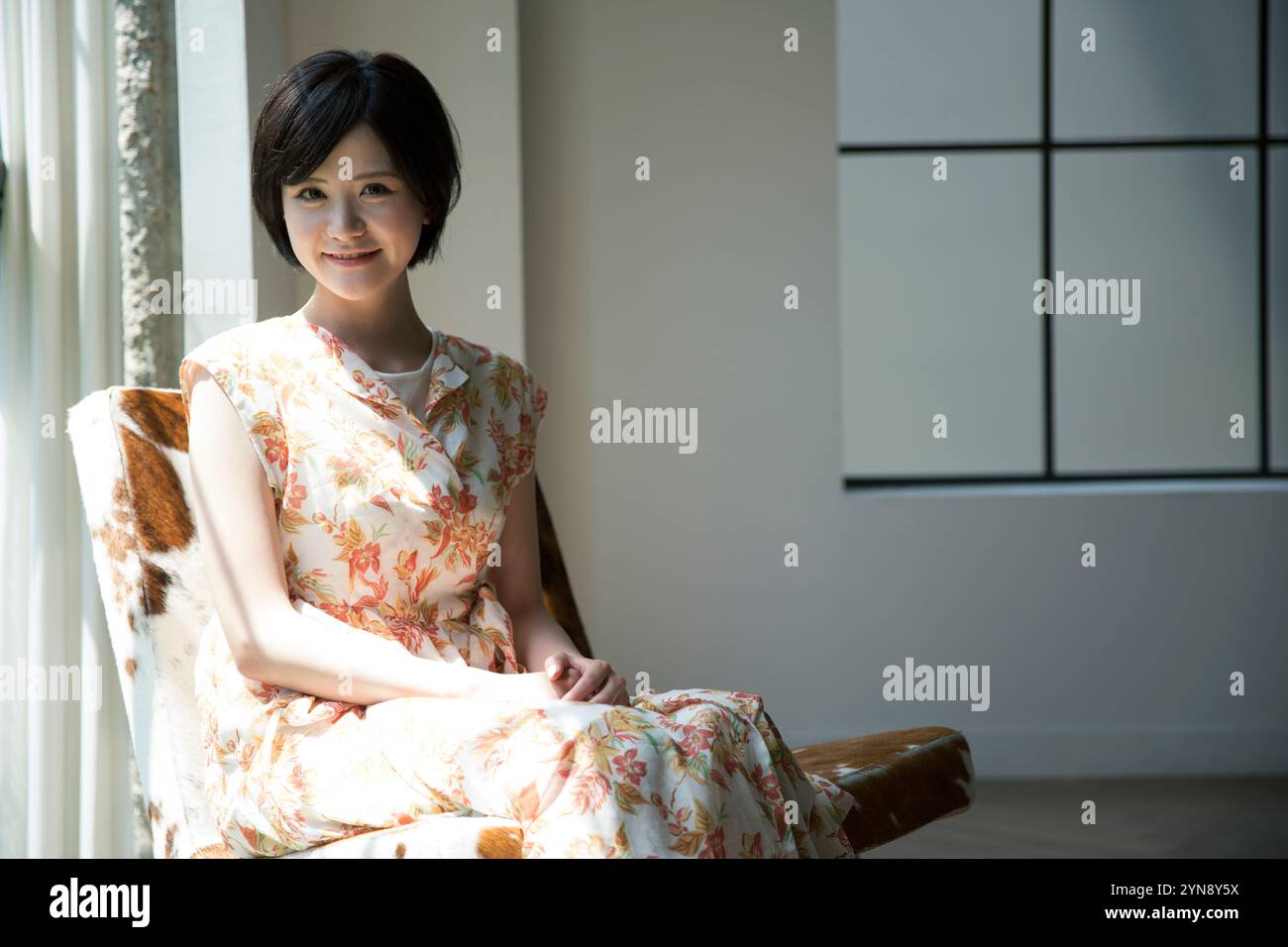 Woman in her 20s in floral one-piece sitting by the window Stock Photo ...