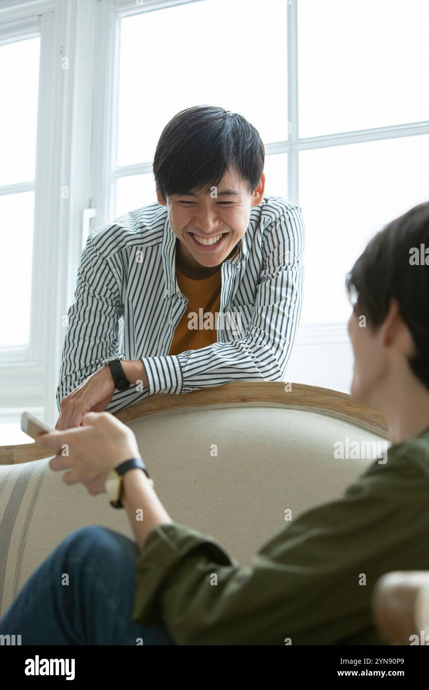 Two men in their 20s sitting on a sofa talking Stock Photo