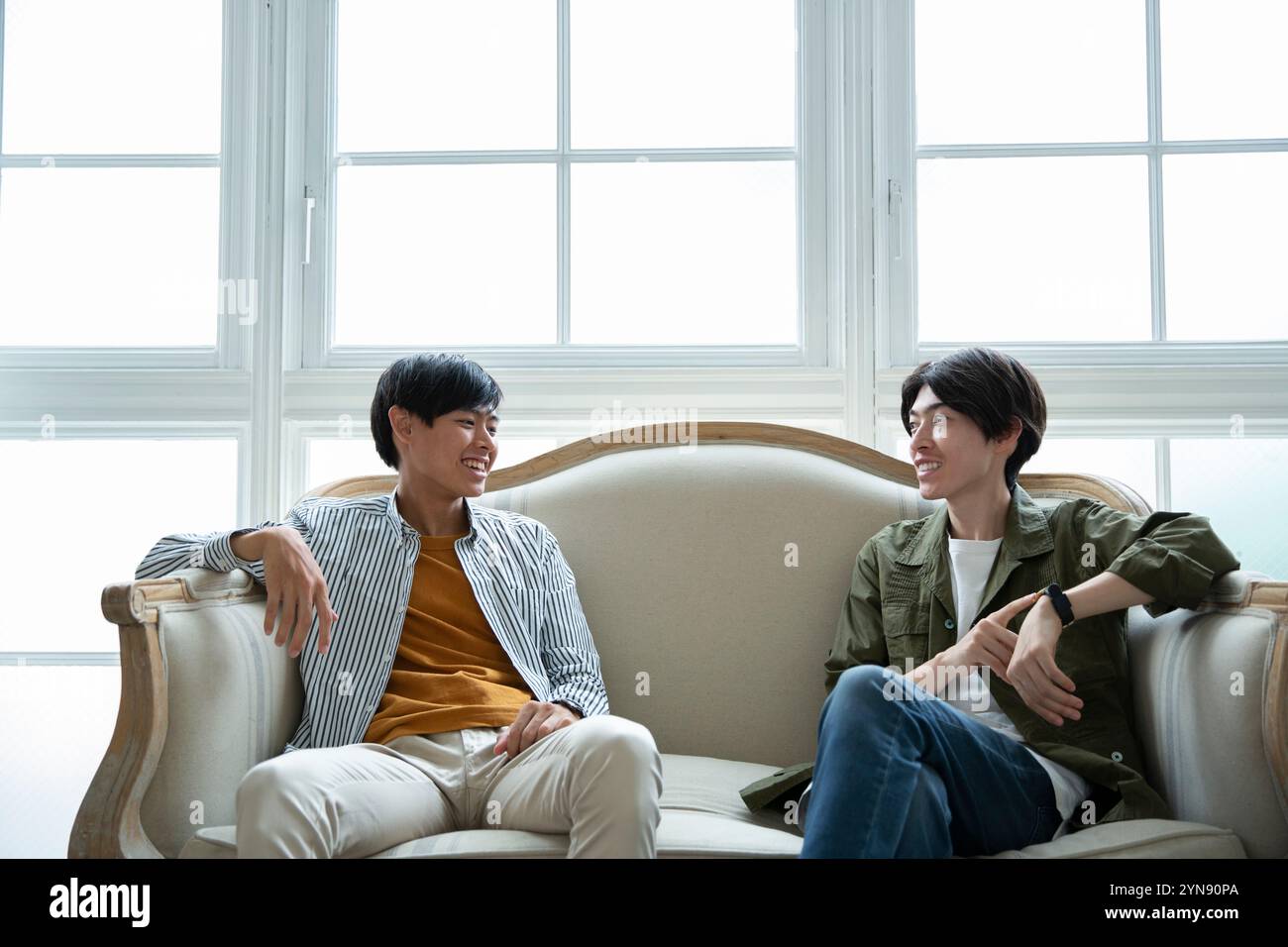 Two men in their 20s sitting on a sofa talking Stock Photo - Alamy