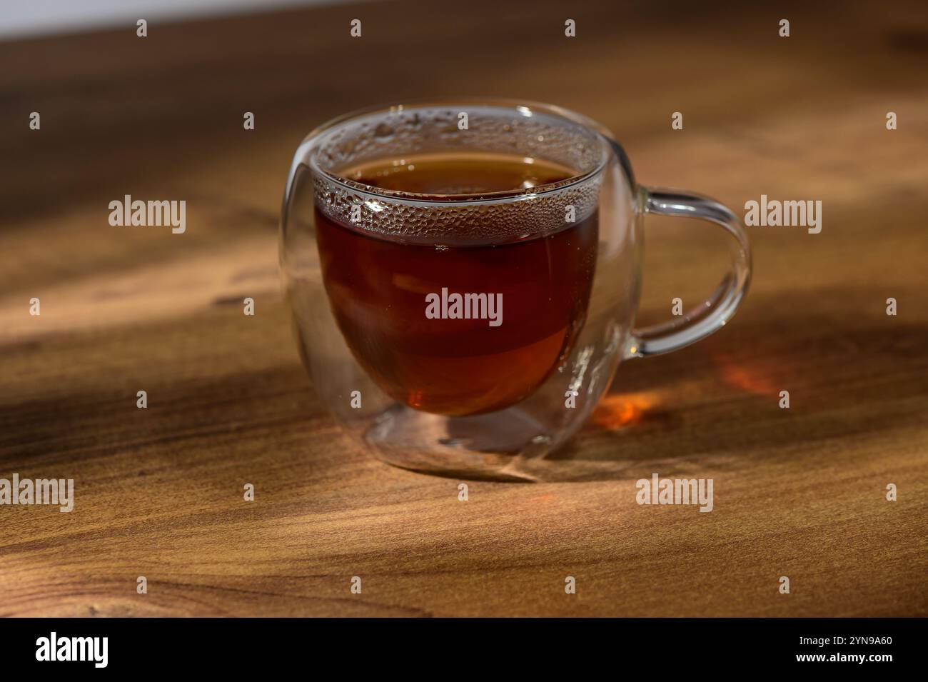 Warmth radiates from a glass cup filled with rich tea, set against the ...