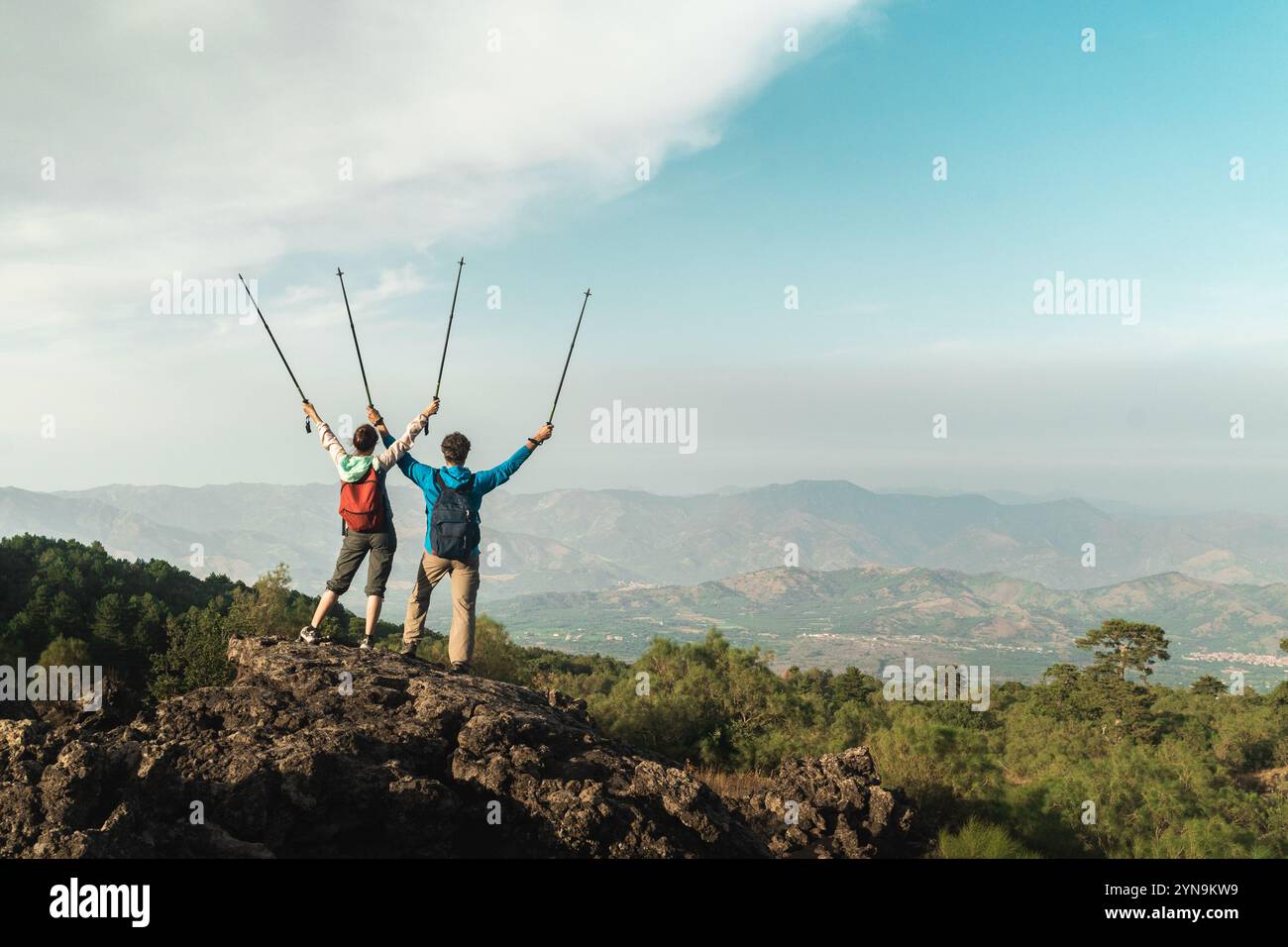 Adult couple celebrating success reaching mountain top together, arms raised in victory. Achievement and adventure lifestyle concept Stock Photo