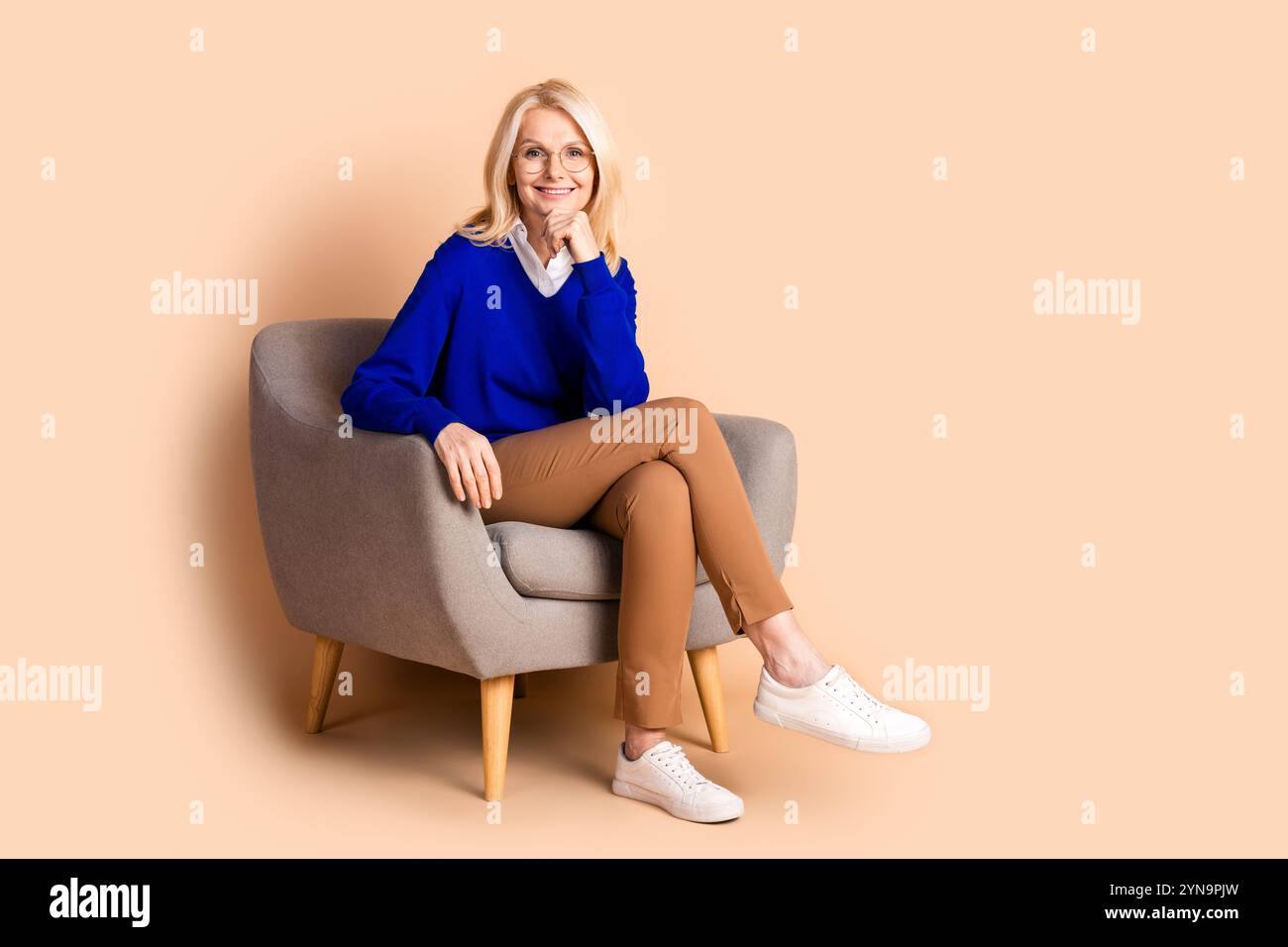 Elegant mature woman sitting comfortably in chair with beige background ...