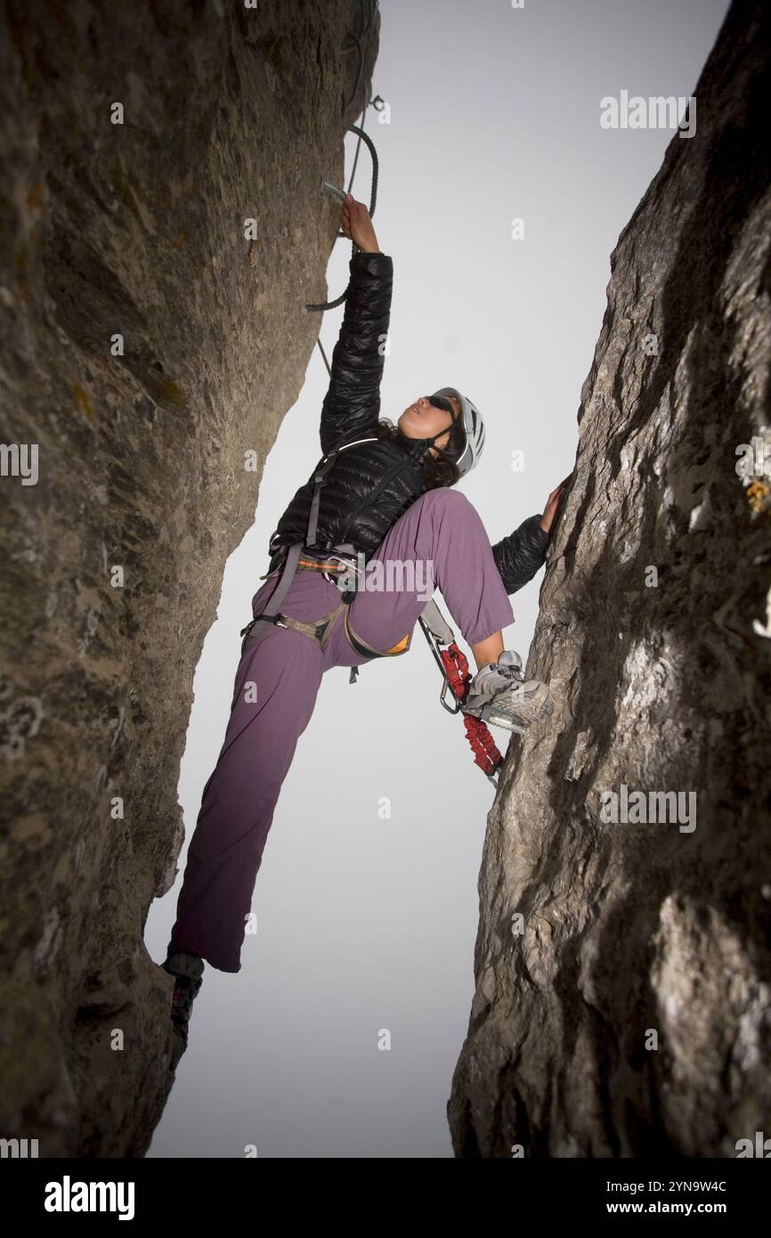 A young woman climbs between two rocks while engaging in the sport of ...