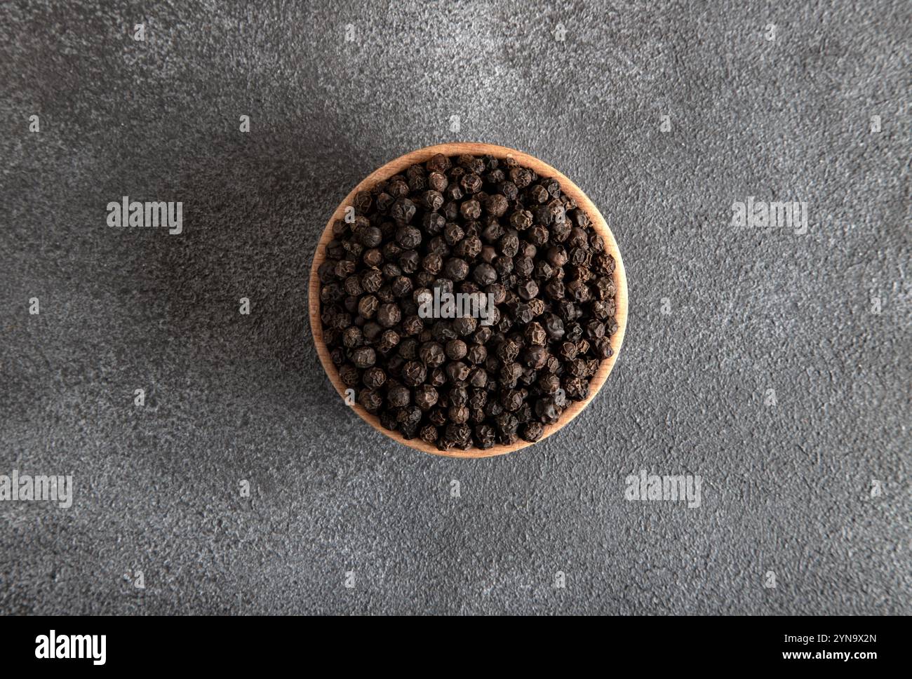 Black peppercorns in wooden bowl on gray concrete background Stock Photo