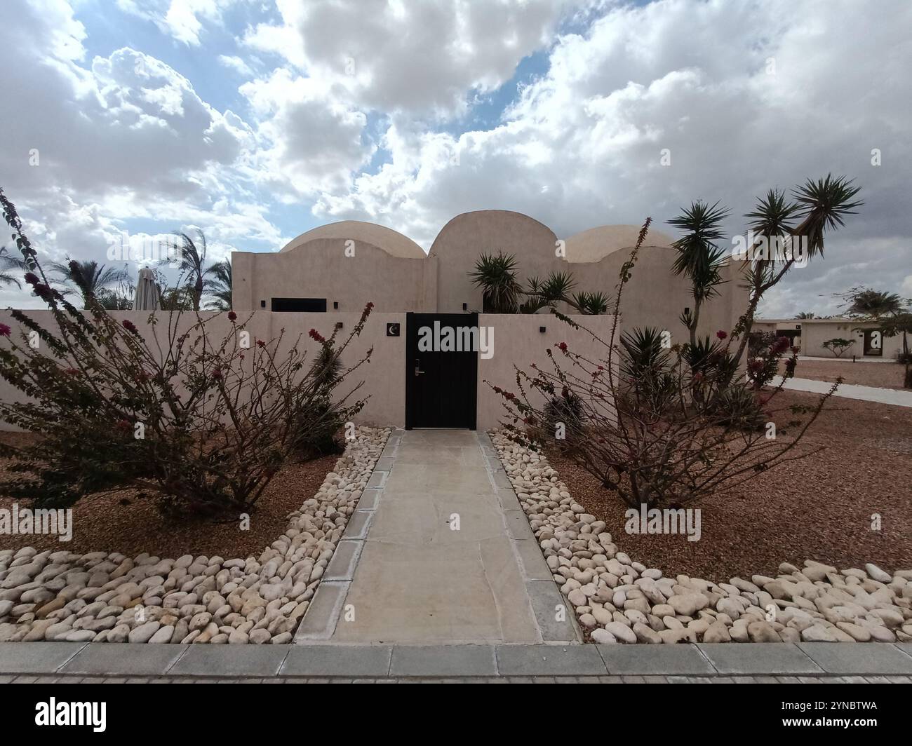 A traditional Bedouin house in the desert, surrounded by trees and a cloudy blue sky, gives the feeling of serenity - Smartphone Captured Stock Image