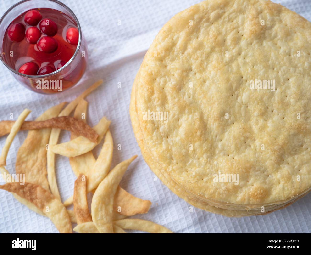Top view over a pile of baked thin round buttery layers, dough scraps on a white waffle towel ready to make a shortcrust puff pastry Napoleon cake. Stock Photo