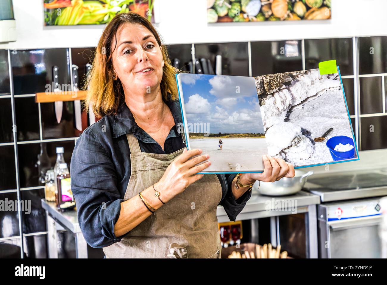 At her cookery school on Djonora Marthaweg, Willemstad, Curaçao, Helmi Smeulders shows a spread from her book *My Curaçao* featuring photographs of the island’s salt pans. Locally sourced sea salt is an integral part of her cooking. Kòrsou, Curacao Stock Photo