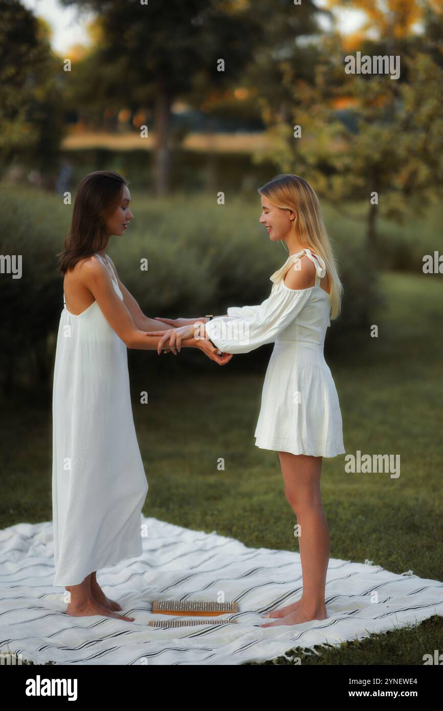 Two women in white dresses holding hands in a serene outdoor setting ...