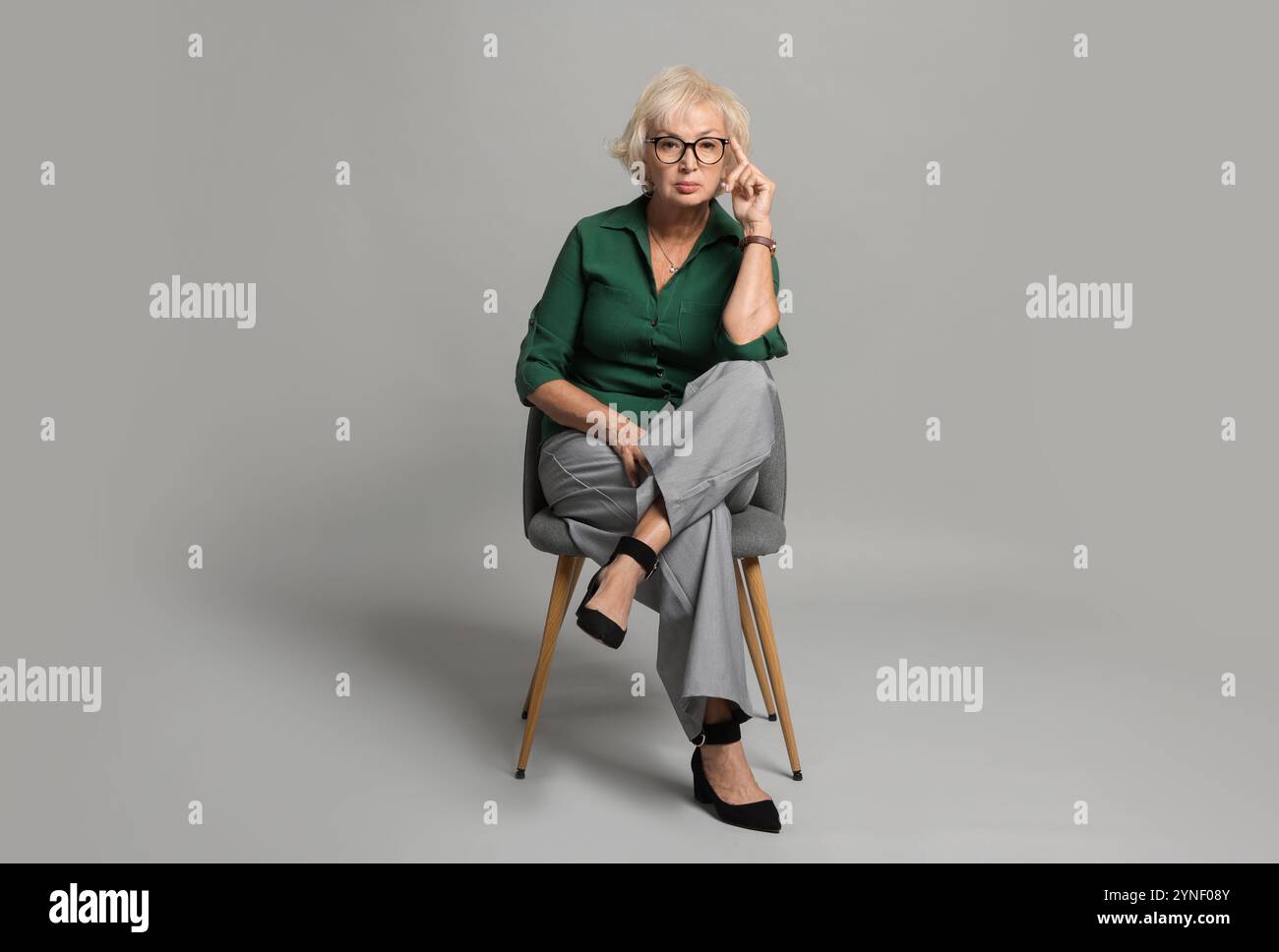 Beautiful senior woman sitting on chair against light grey background ...