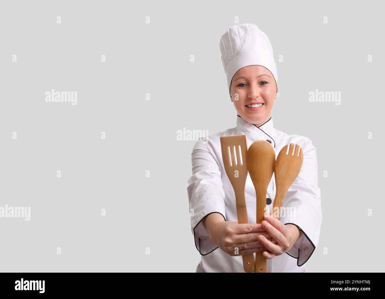 Professional female chef holding wooden kitchen utensils and smiling on white background Stock Photo