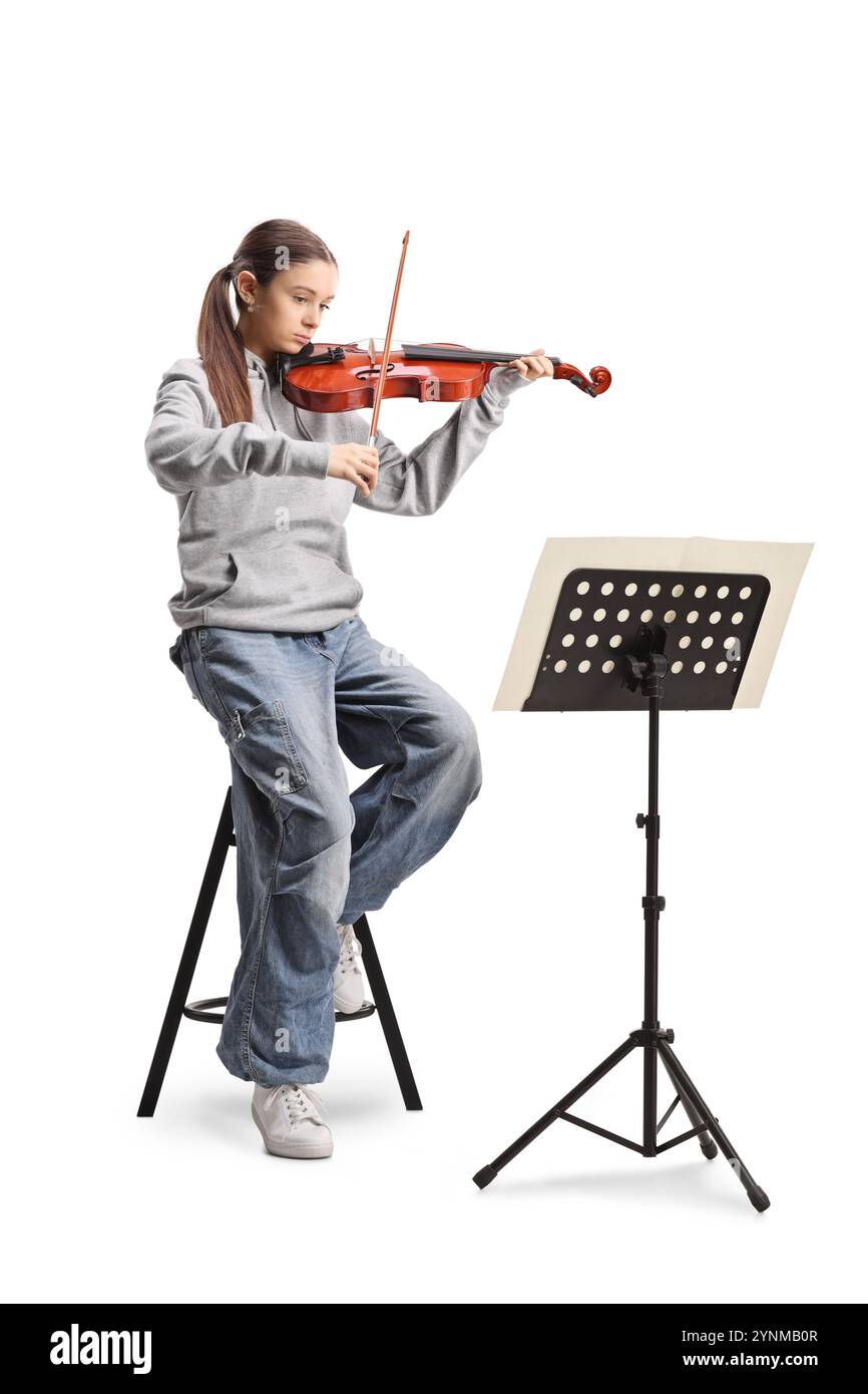 Teenage girl sitting on a chair and playing a violin with a music stand ...