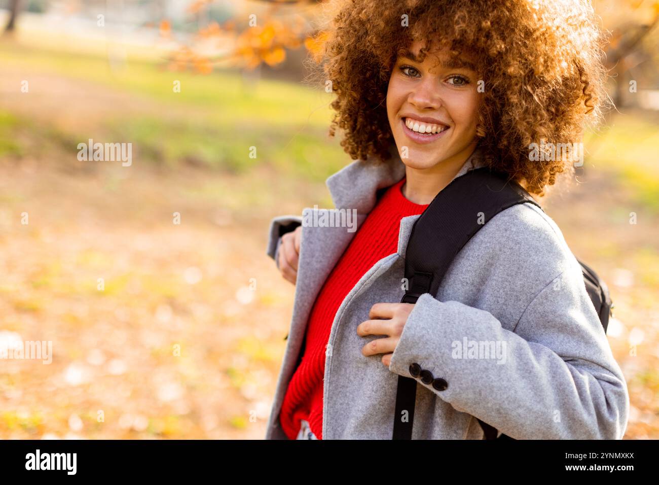 In a beautiful autumn park, a joyful young woman with curly hair ...