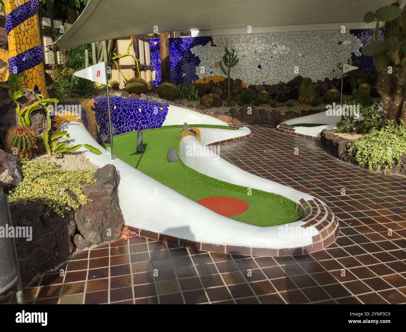 This vibrant indoor mini golf area showcases a distinct design with colorful elements. The well maintained green and artistic landscaping provide a fu Stock Photo