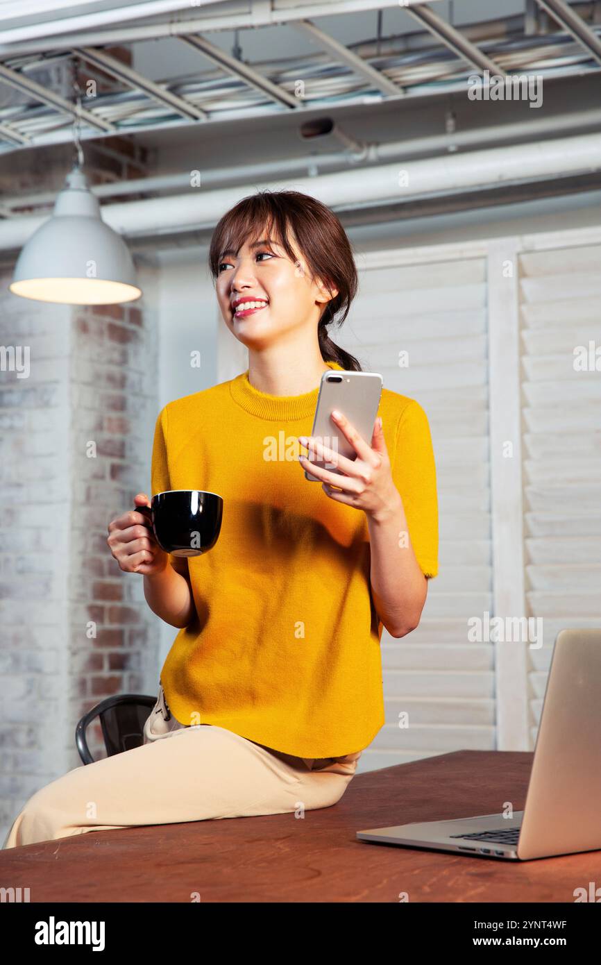 Woman in her 20s sitting at a desk operating a smartphone Stock Photo