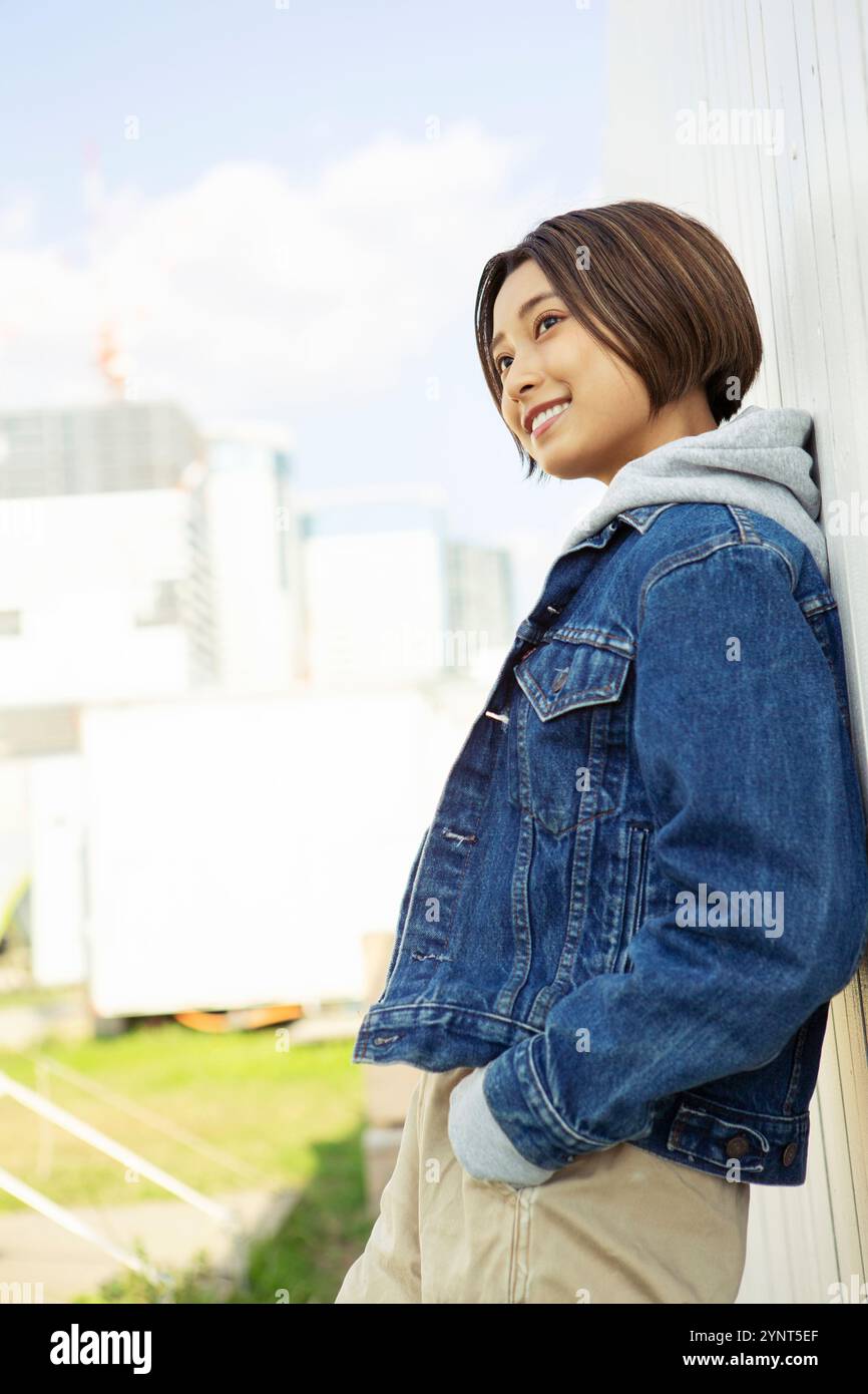 Smiling woman in her 20s leaning against wall Stock Photo - Alamy