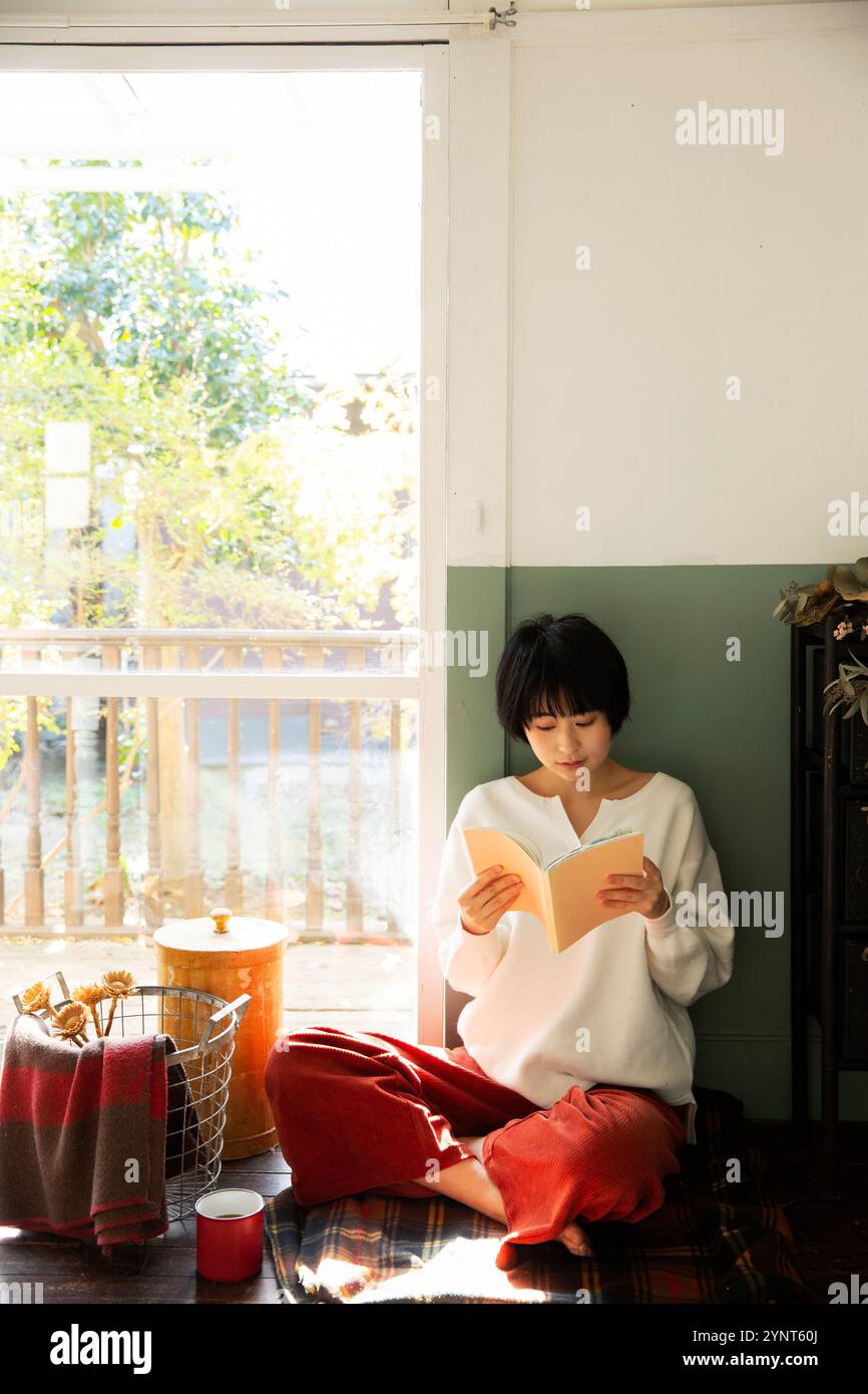 Woman in her 20s reading a book by the window Stock Photo - Alamy