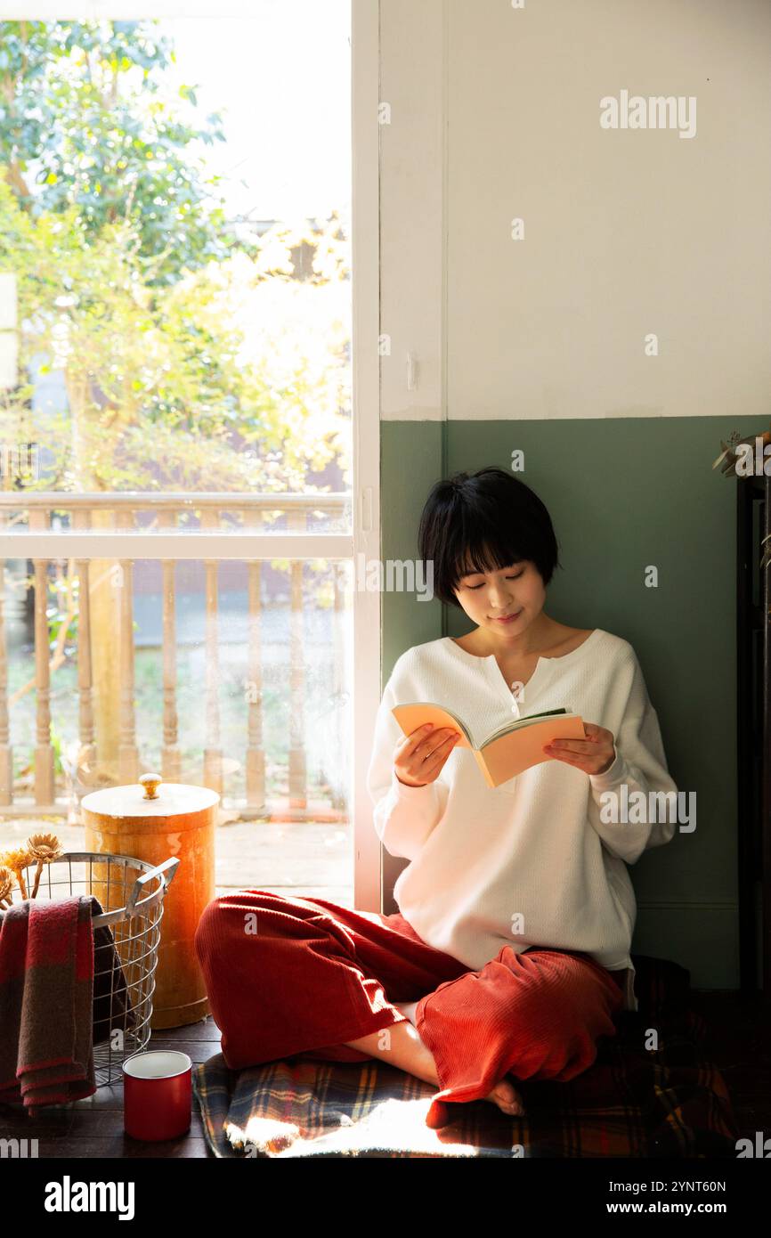 Woman in her 20s reading a book by the window Stock Photo - Alamy