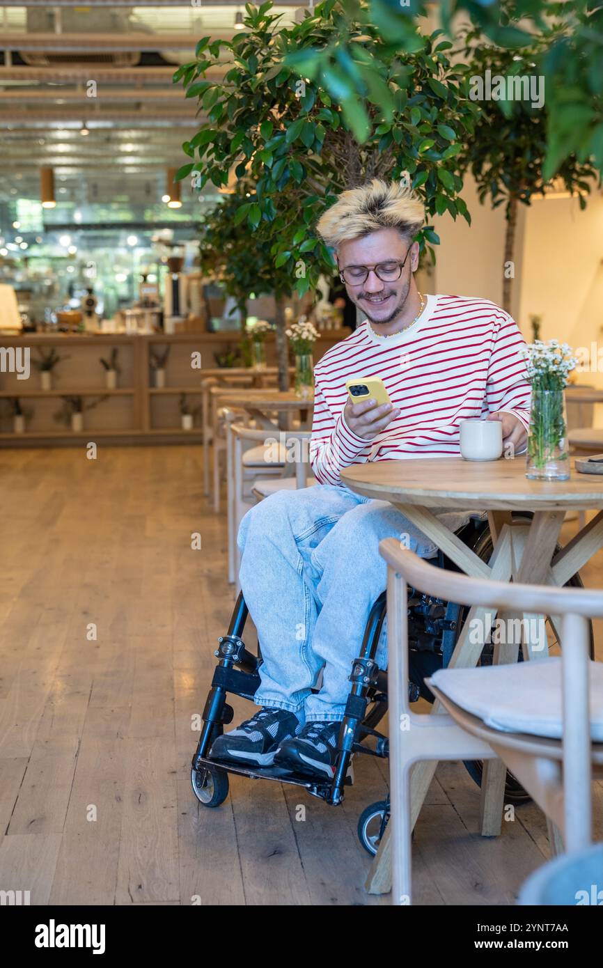 Smiling dreamy freelancer man drinking coffee at cafe table, using mobile phone. Coffee break. Stock Photo