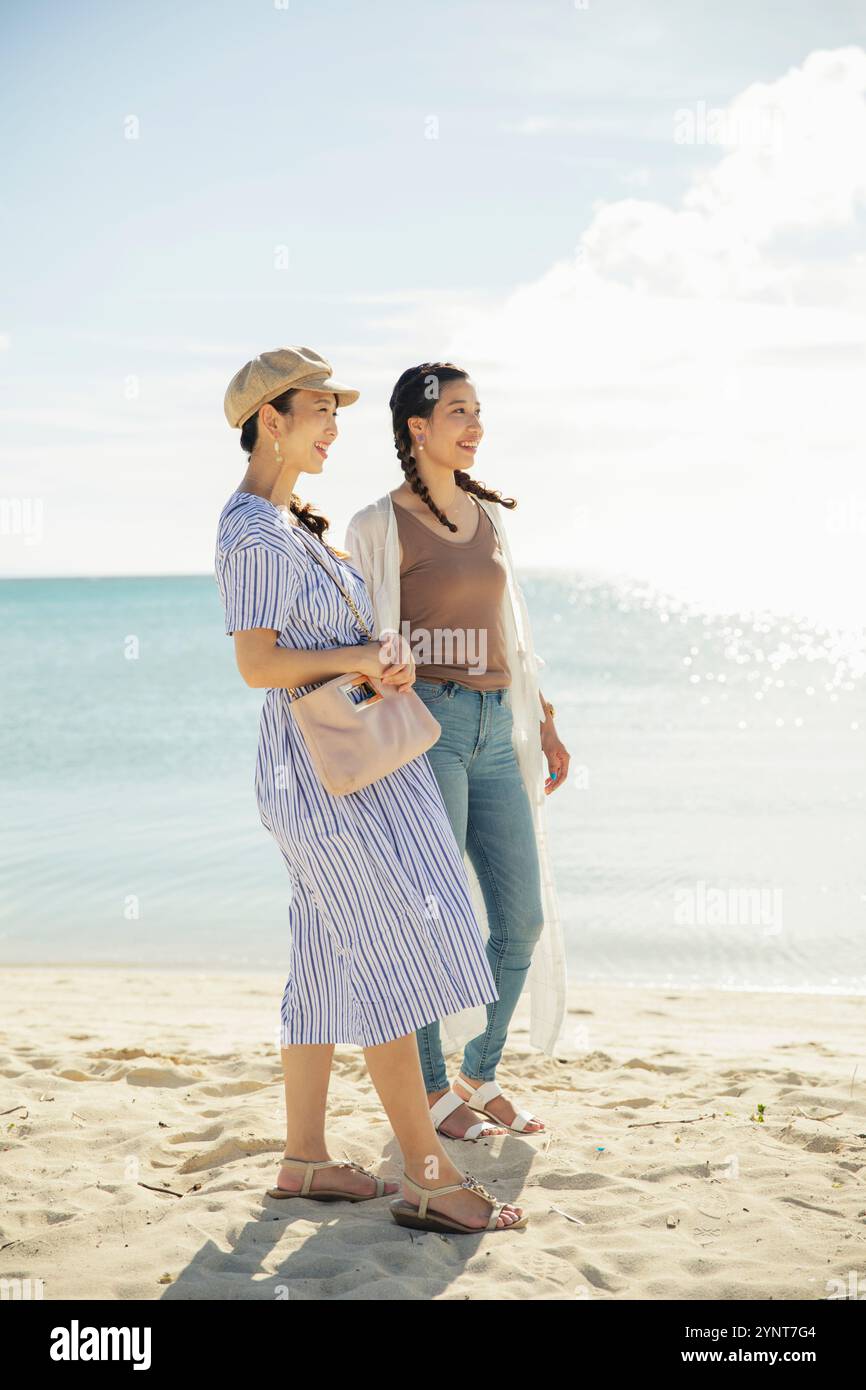 Two women in their 20s walking on a sandy beach Stock Photo - Alamy