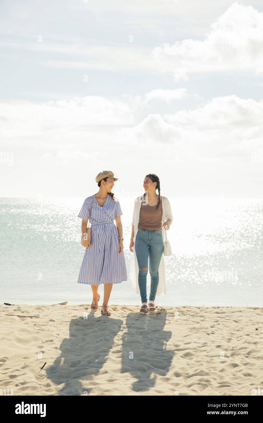 Two women in their 20s walking on a sandy beach Stock Photo - Alamy