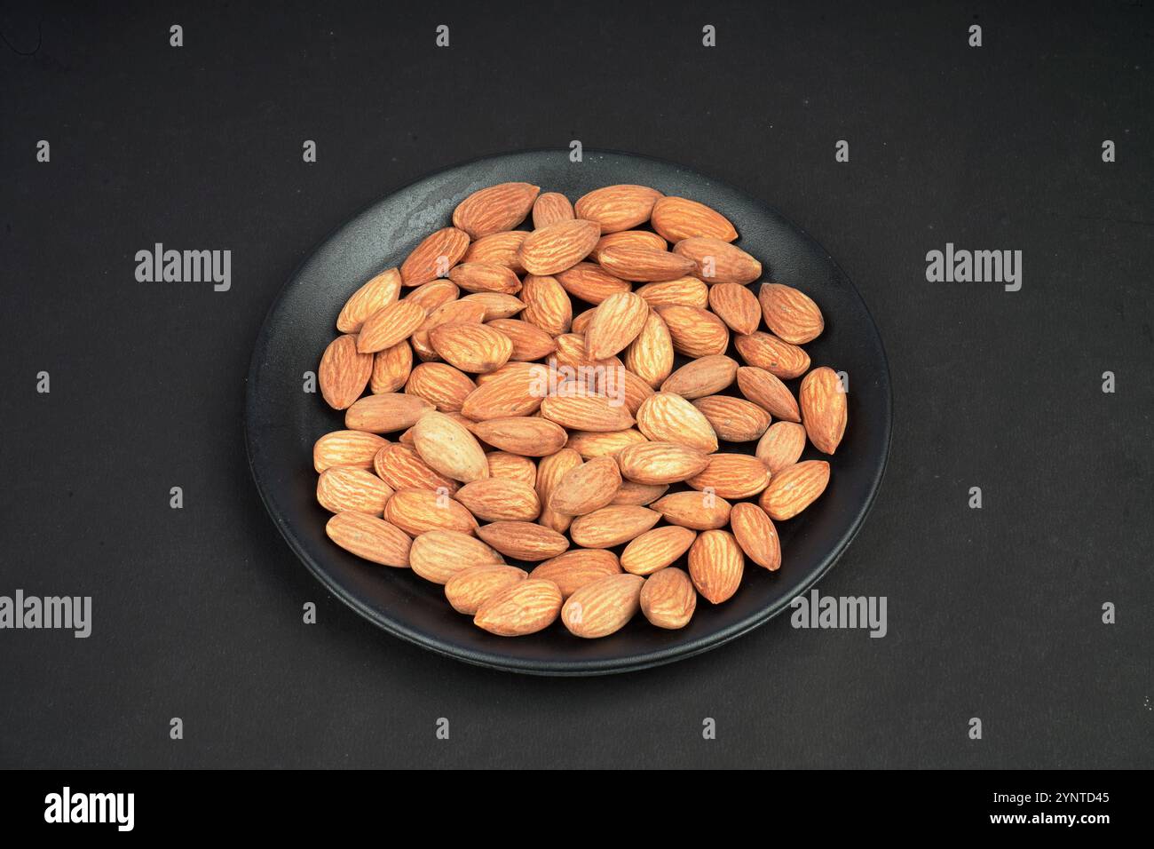 Fresh almonds in a black flat plate Stock Photo