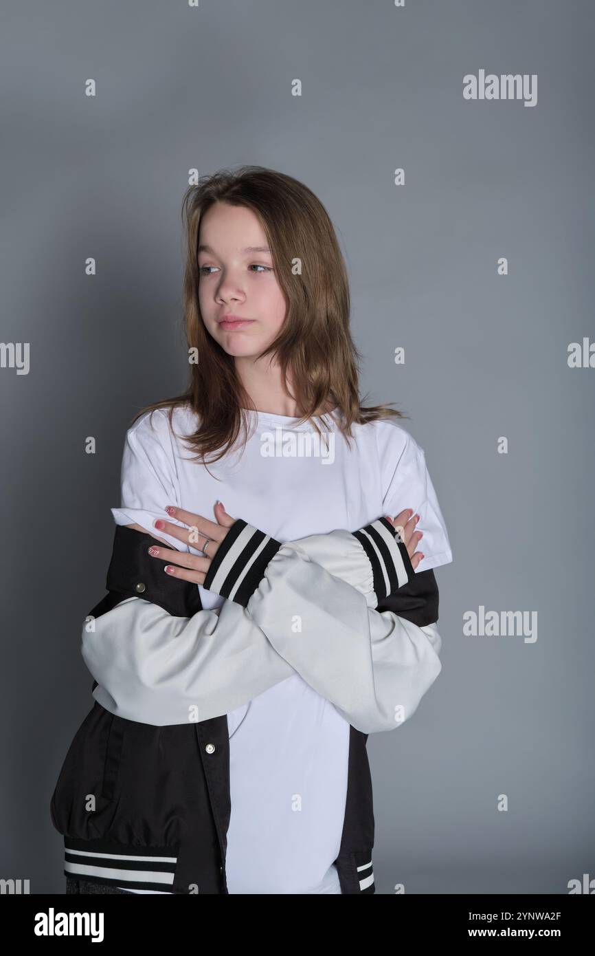 A teenage girl strikes a casual pose wearing jeans and a varsity