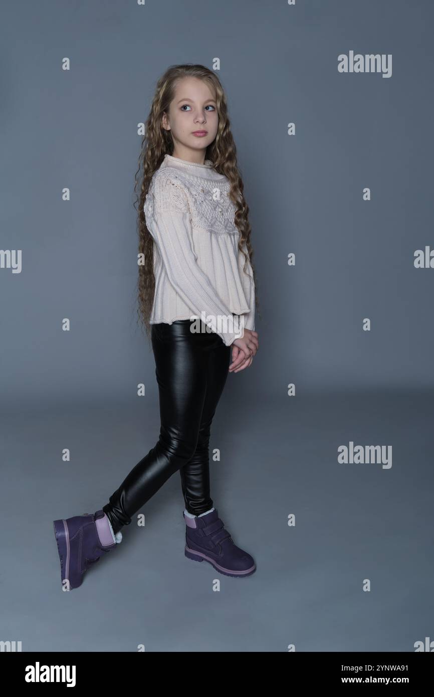 The young girl stands with a hand on her hip, gazing forward with a ...