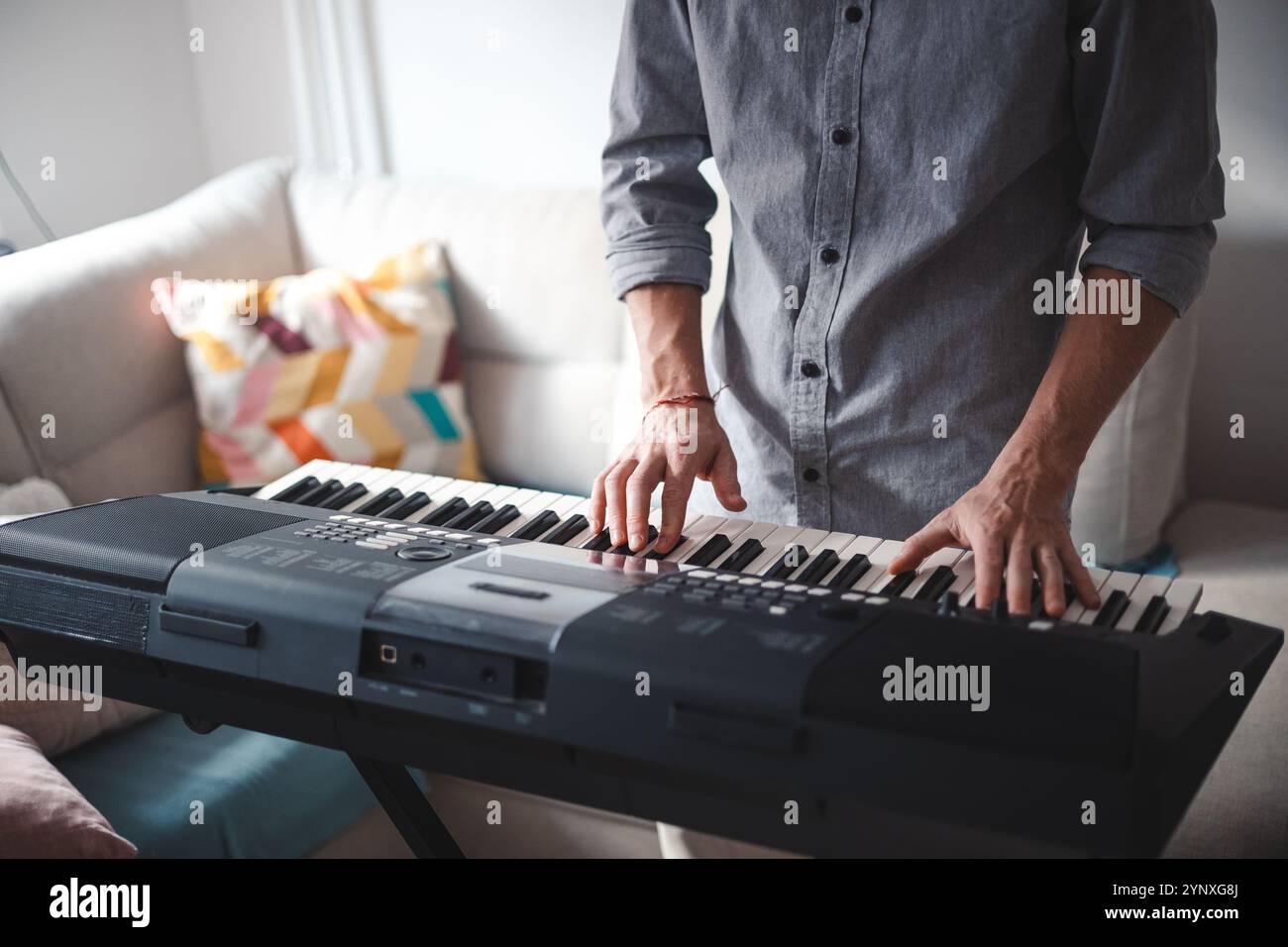 Musician's hands actively playing a digital keyboard, blending focus and creativity in a modern home setting with soft lighting and minimalist decor. Stock Photo