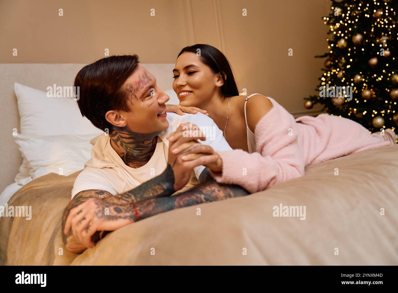 Loving couple enjoys warm cuddles on a soft bed under the glow of Christmas lights Stock Photo