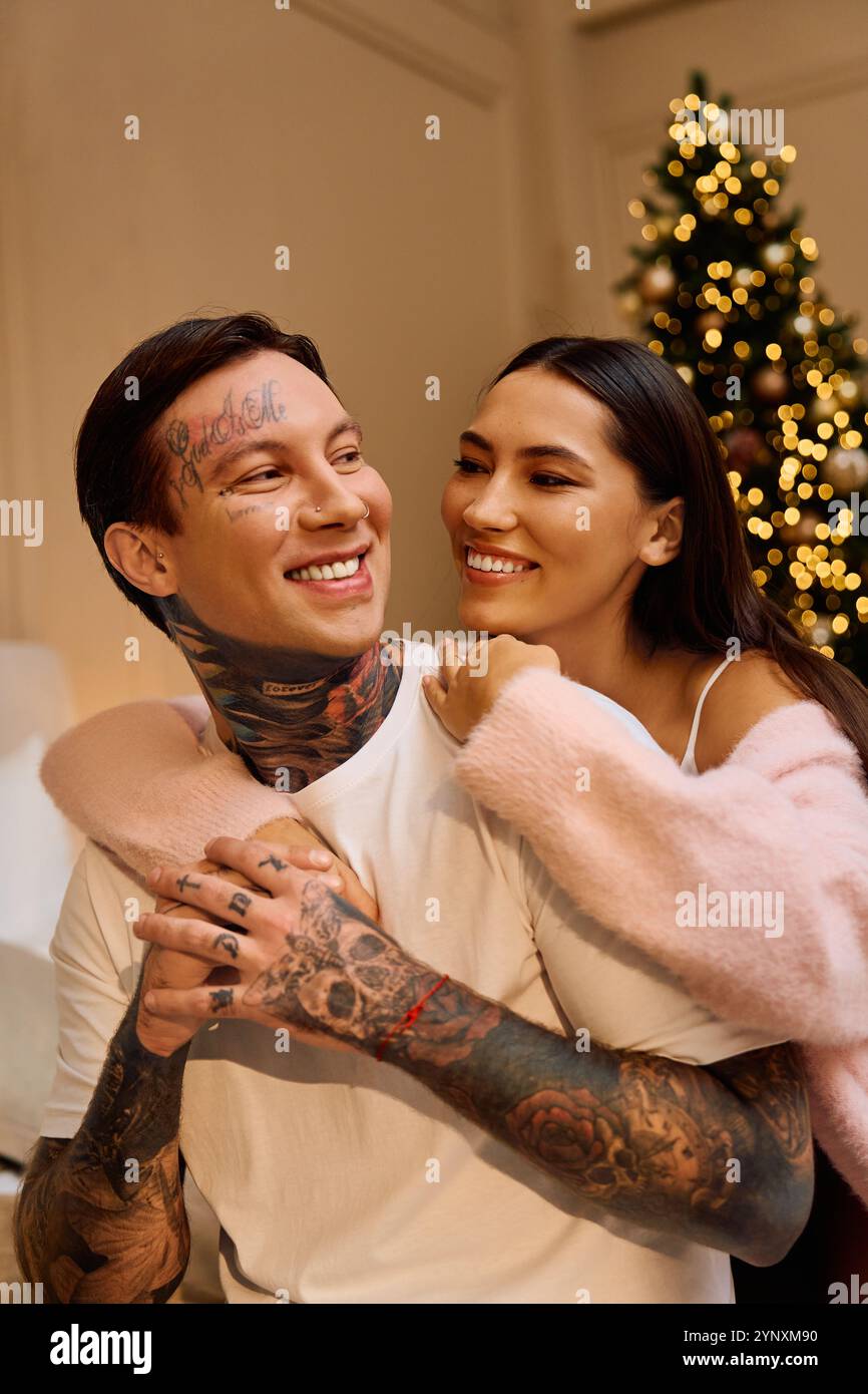 Two young lovers embrace warmly while smiling by the festive lights of a holiday tree. Stock Photo