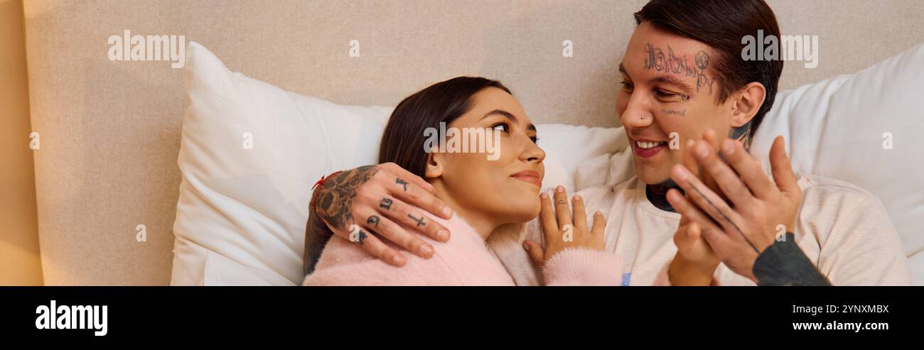 A couple cuddles on a soft bed, exchanging loving glances and laughter, embracing their bond. Stock Photo