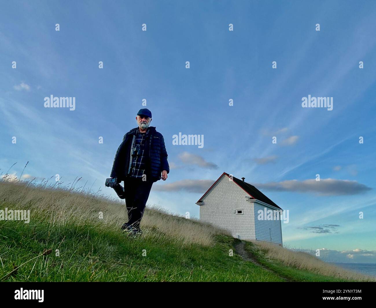 Man with a long lens camera walking down a hill away from a house on a coastal hillside, Saturna Island, Southern Gulf Islands, British Columbia, Canada Stock Photo