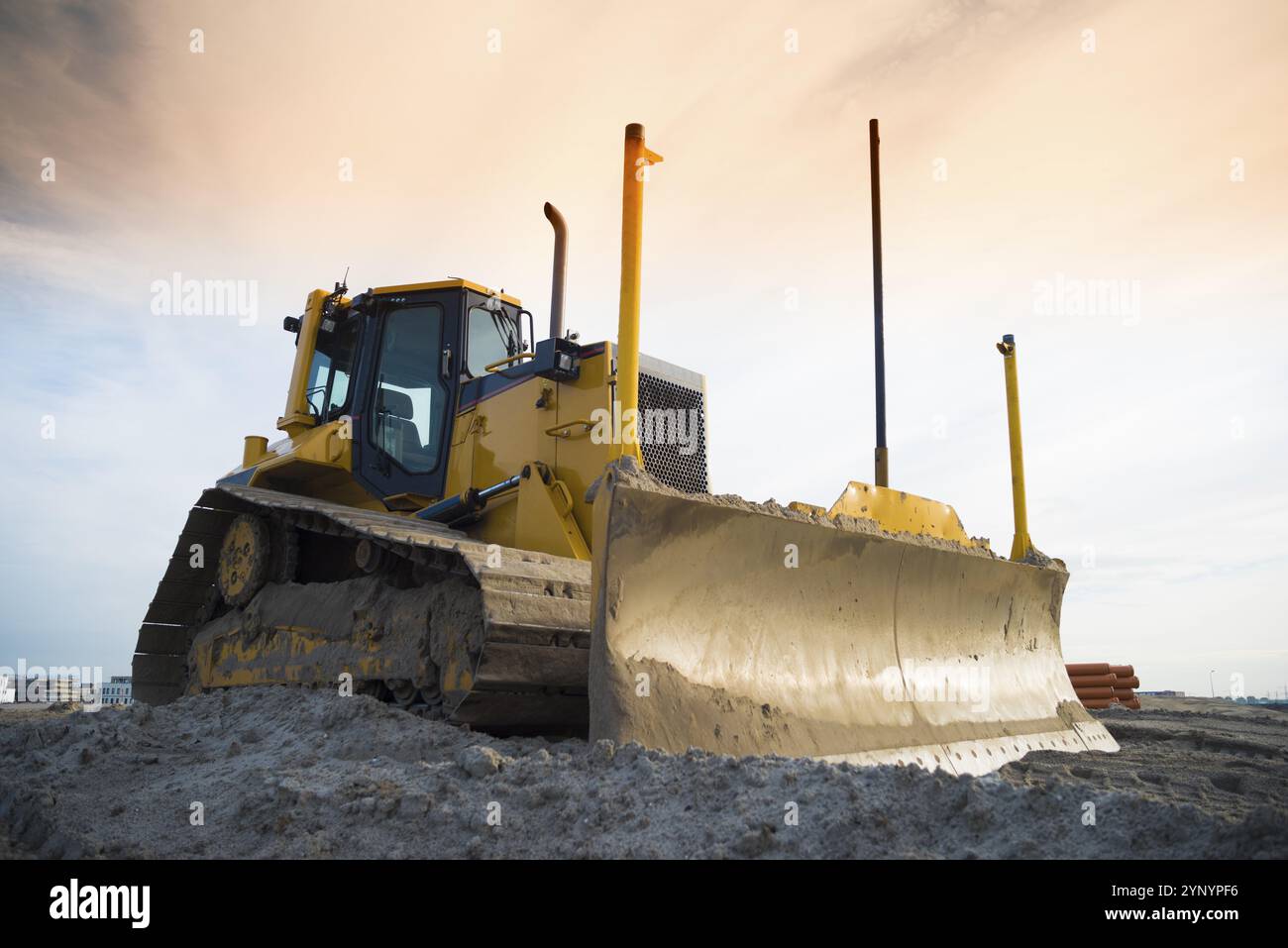 Yellow excavator on a construction site in front of an orange sky Stock Photo