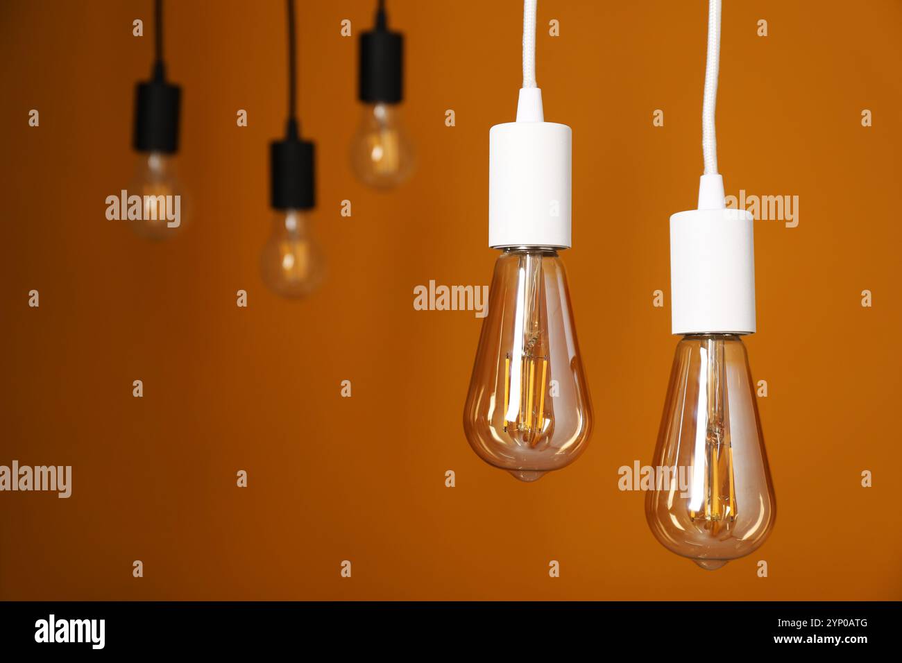 Light bulbs hanging on cords against orange background Stock Photo