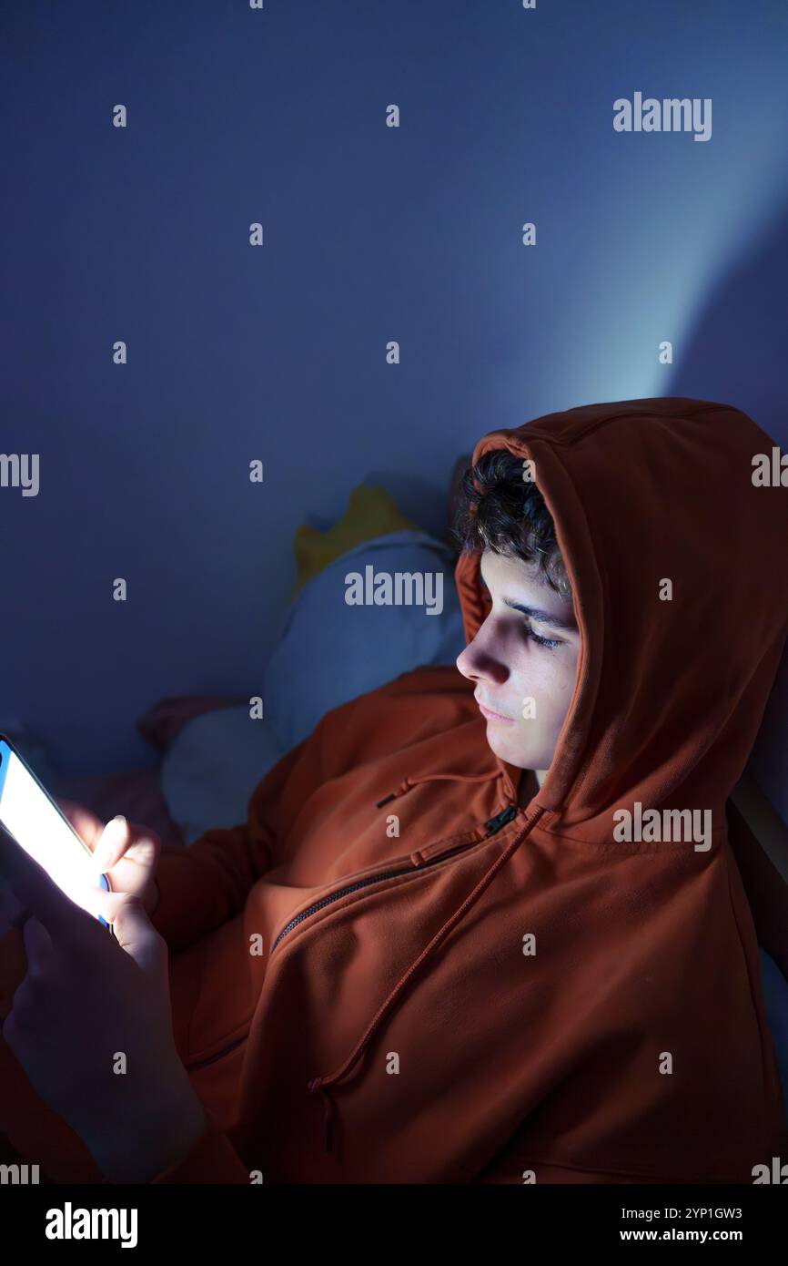 Teenager using mobile phone in bed at night, illuminated by screen light Stock Photo