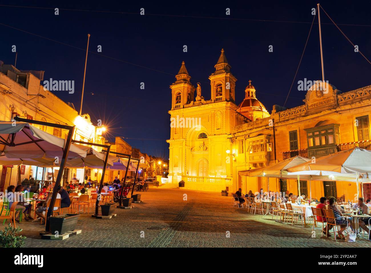 Dining out al fresco on the town square by the Parish Church in the popular fishing village of Marsaxlokk, Malta Stock Photo