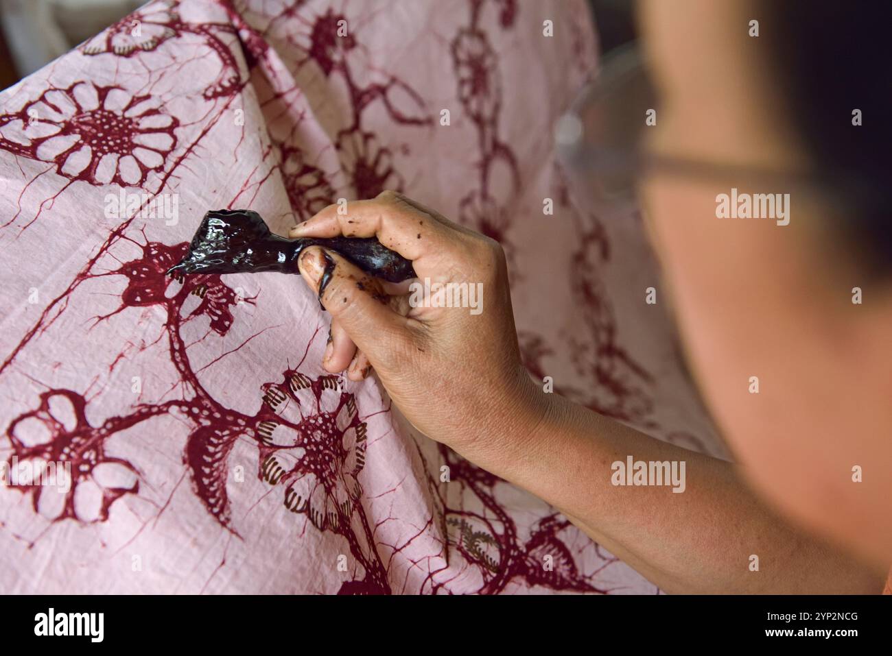 Woman using a pen-like tool (canting) to apply liquid hot wax to create pattern on the fabric before dyeing, workshop of Kidang Mas Batik House, Lasem Stock Photo
