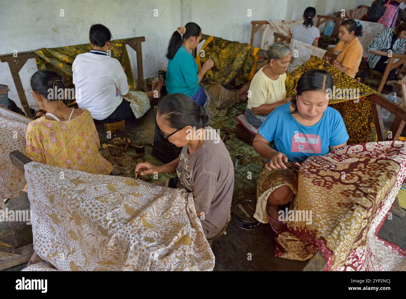 Women using a pen-like tool (canting), to apply liquid hot wax to create pattern on the fabric before dyeing, workshop of Kidang Mas Batik House Stock Photo