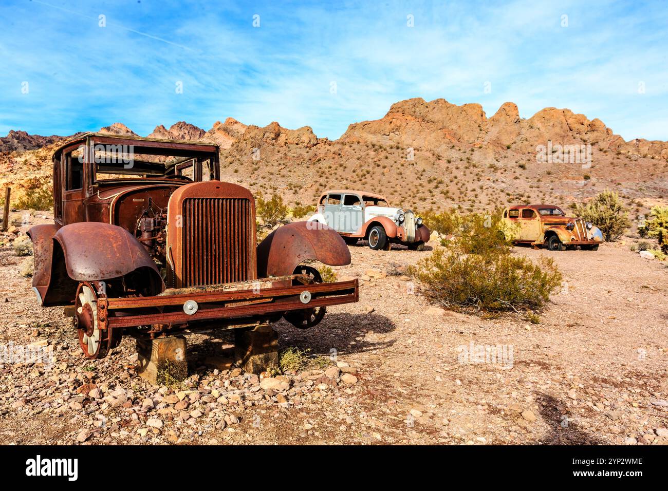 A rusted old car is parked in the desert. The car is surrounded by a ...
