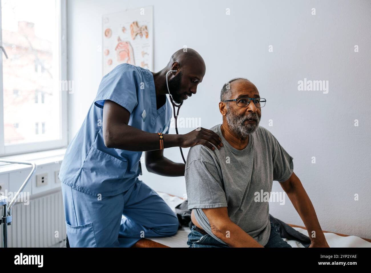 Male medical professional checking senior man's back with stethoscope in examination room at clinic Stock Photo