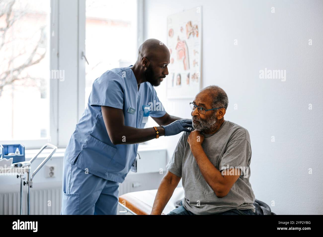 Male medical expert checking neck of senior patient sitting on bed in ...
