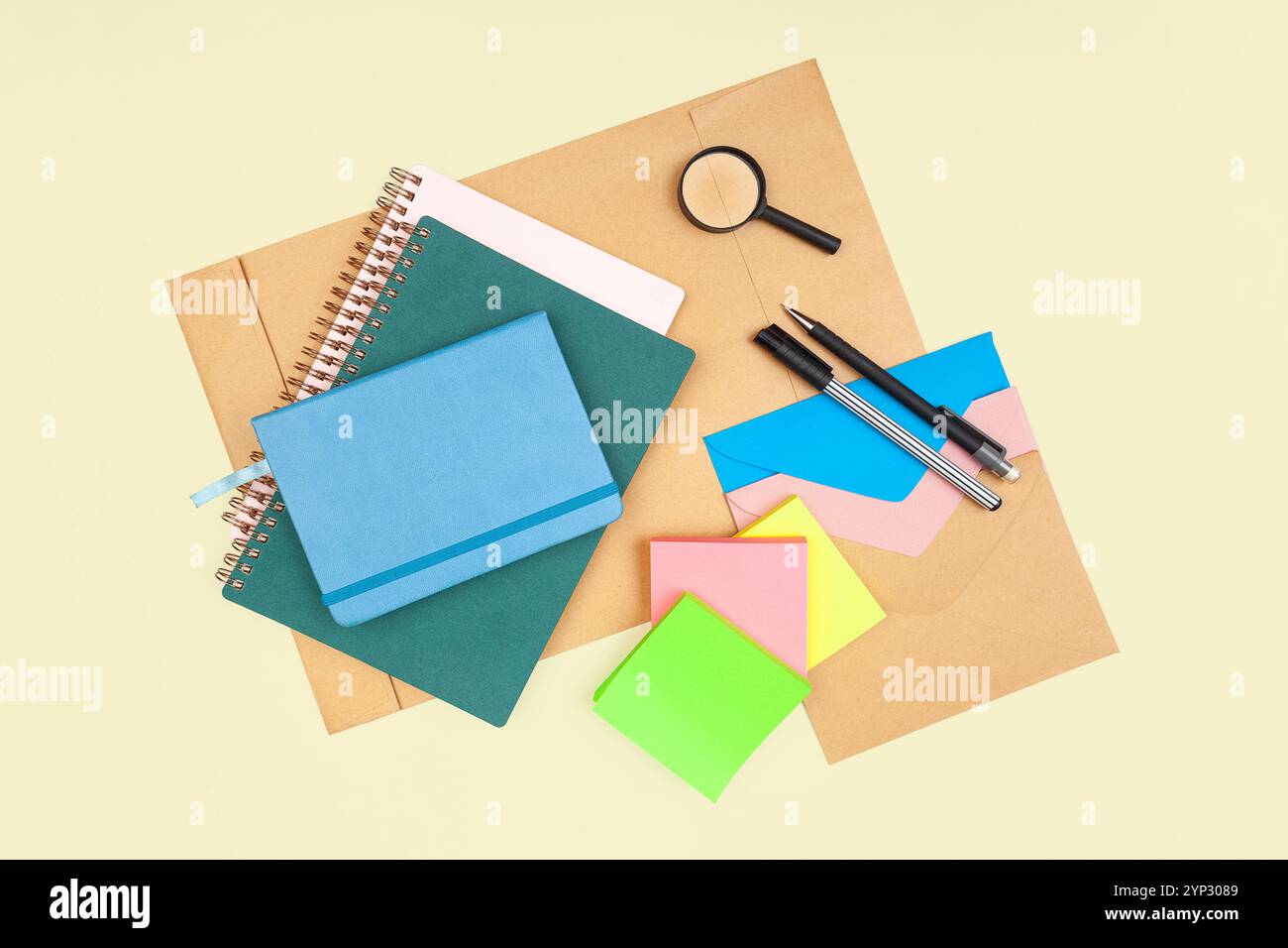 Office and school supply on a light yellow background. Notebooks, pen, pencil, envelopes, stickers, magnifier. Top view. Stock Photo