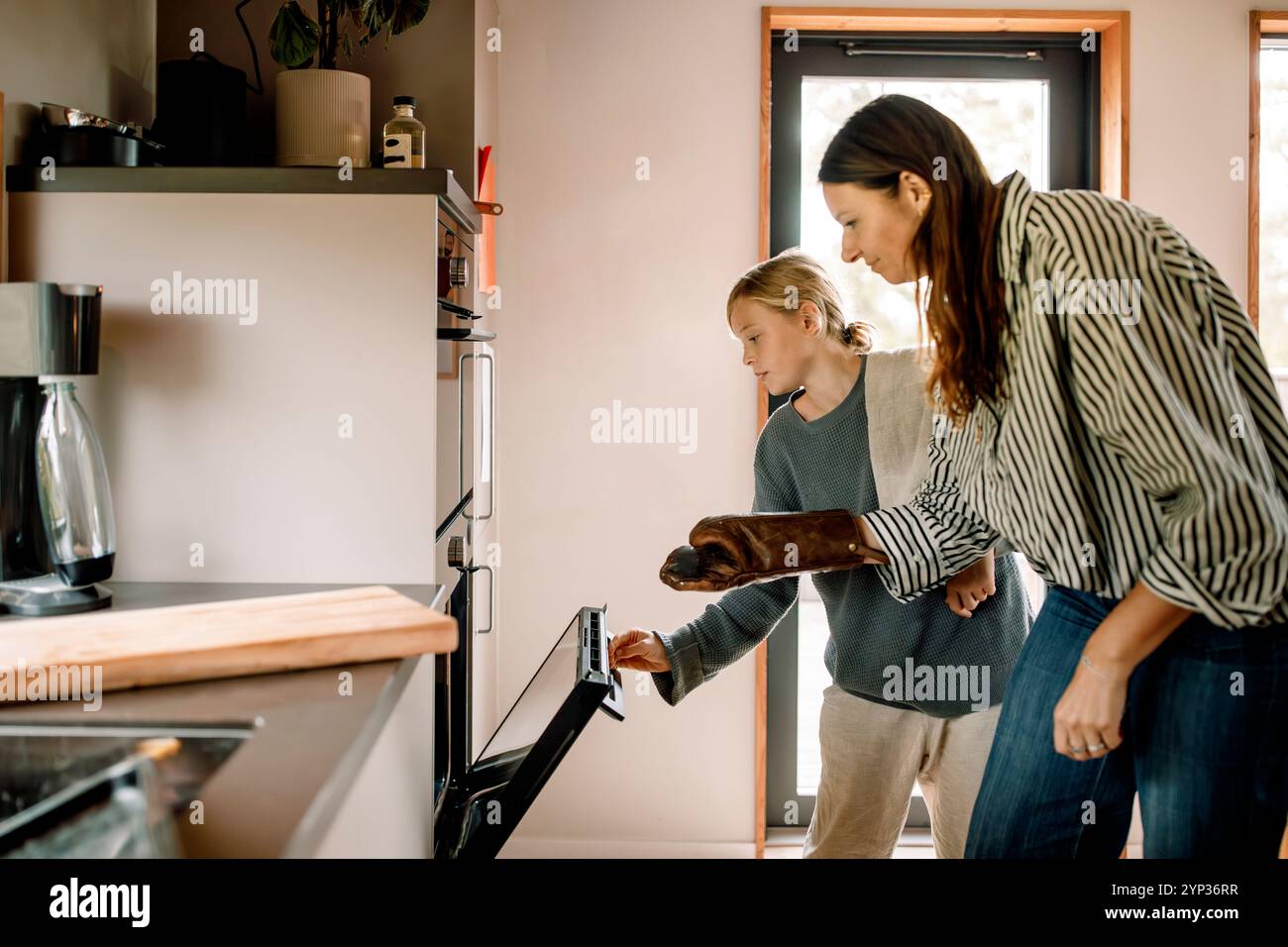 Woman wearing mitt while son opening oven in kitchen at home Stock Photo