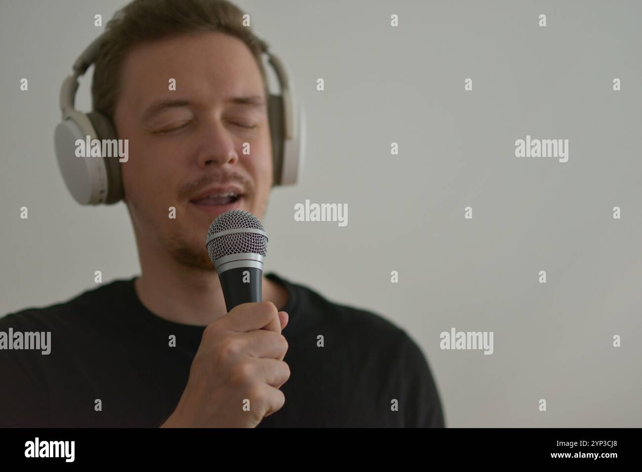 A man wearing headphones emotionally singing in microphone with eyes closed. Blurred image with focus on a hand foreground. Stock Photo